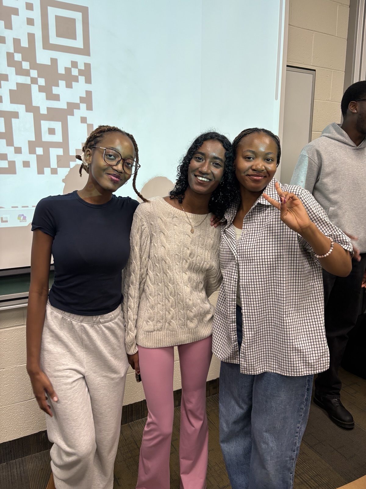 Three members posing together in front of a projector screen